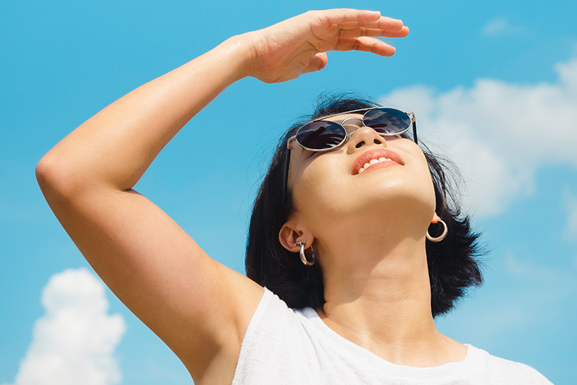 A woman in sunglasses and a white tank top enjoys the sun, highlighting the importance of vitamin D for health.