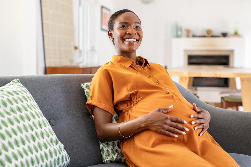 A pregnant woman sits on a couch, reflecting on the importance of B12 and folate for a healthy pregnancy.