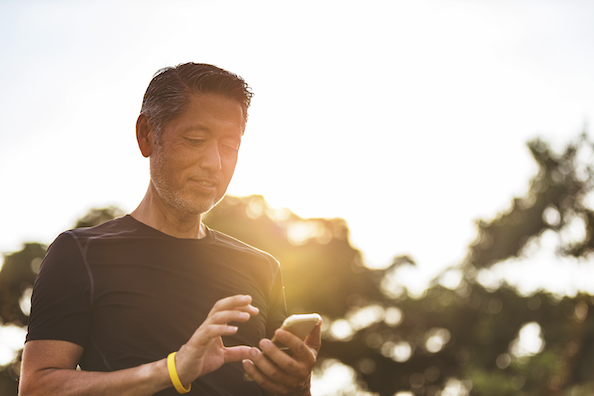 A man stands in the sun, engaged with his phone, highlighting a moment of leisure and checking on routine health tests.