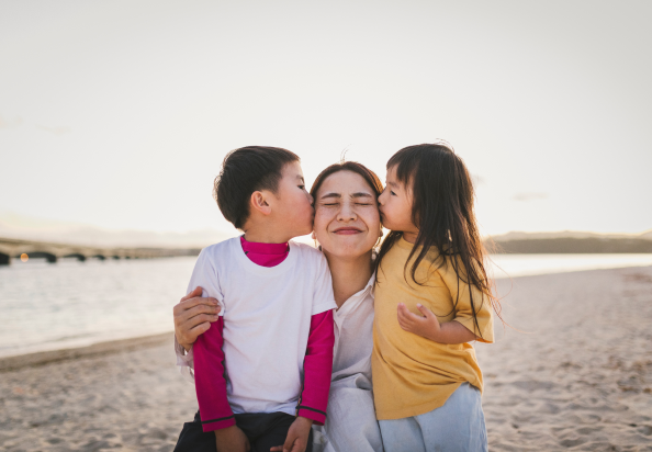 A woman and two children enjoying a sunny day at the beach, playing in the sand and splashing in the waves.