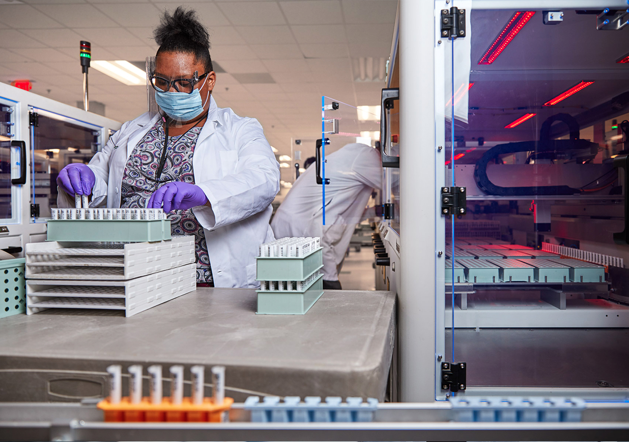 A woman wearing a lab coat and mask is engaged in operating a machine, showcasing her dedication in a lab environment.