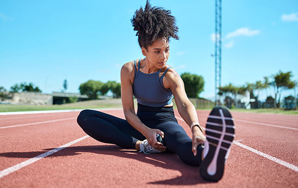 A woman stretches on a running track, promoting heart health awareness during Heart Health Month