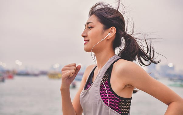 A young adult woman running with headphones listening to a podcast on women’s health testing. 