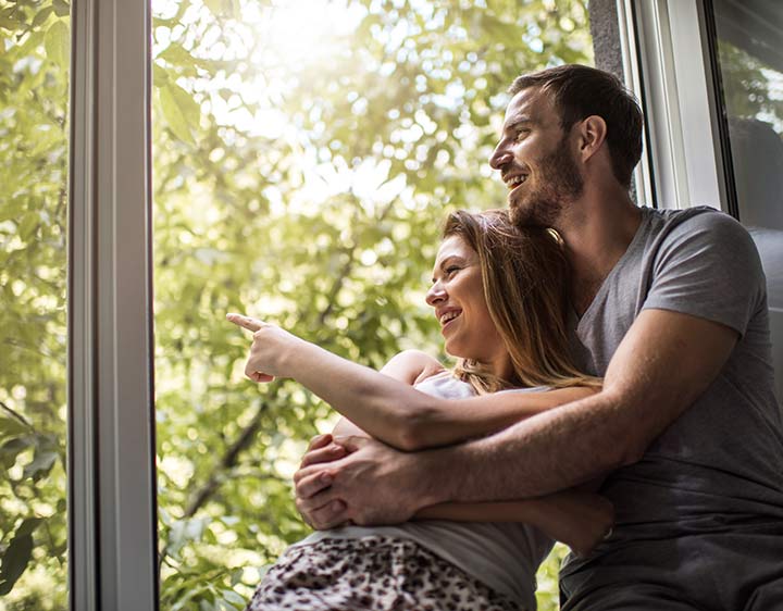 A couple sitting in the window of their home, breathing fresh air.