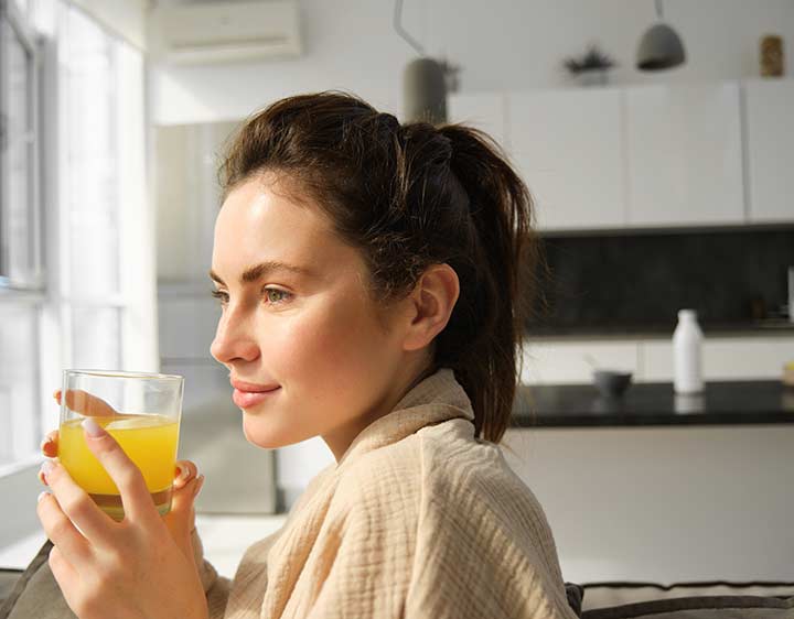 A woman sitting and holding a glass of orange juice looking out the window