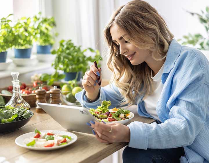 A woman eating a vegan meal checks her health test results on a tablet.
