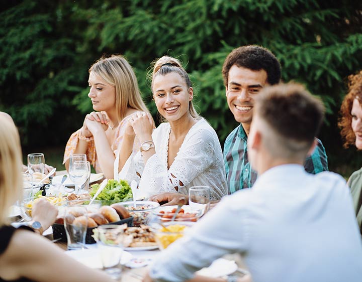 People gathered around an outdoor dining table enjoying a meal in a garden setting.
