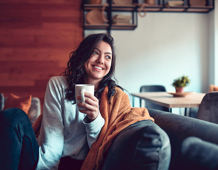 A woman smiles while resting and drinking tea while having mono.