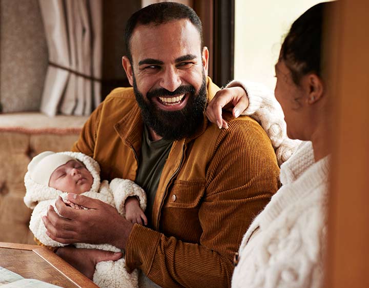 A man smiles while holding a newborn baby