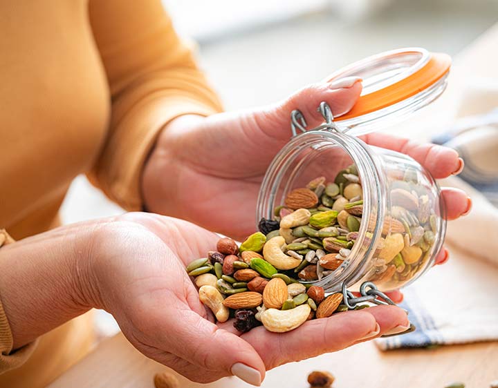 close up of a womans hand pouring a mixed jar of tree nuts into her hand to eat. 
