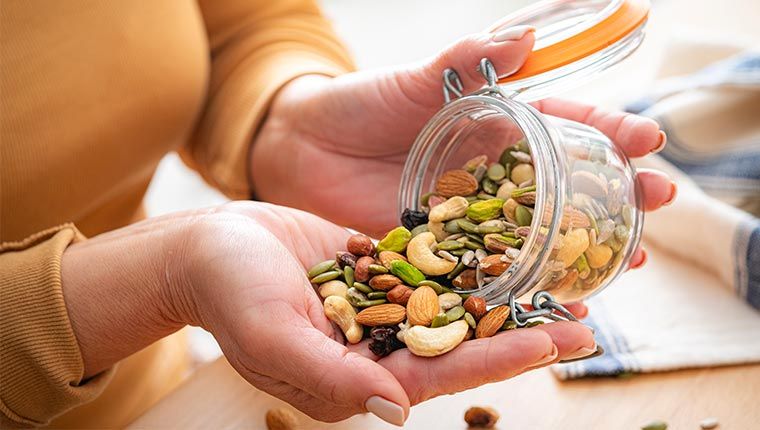 Close up of a womans hand pouring a mixed jar of tree nuts into her hand to eat.