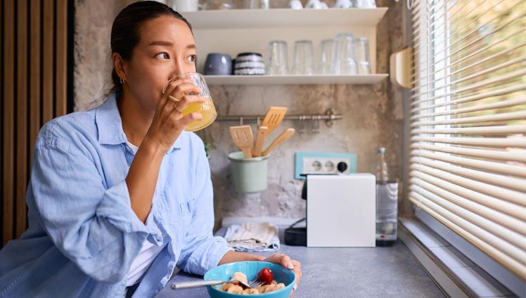 Woman drinking orange juice looking out window.