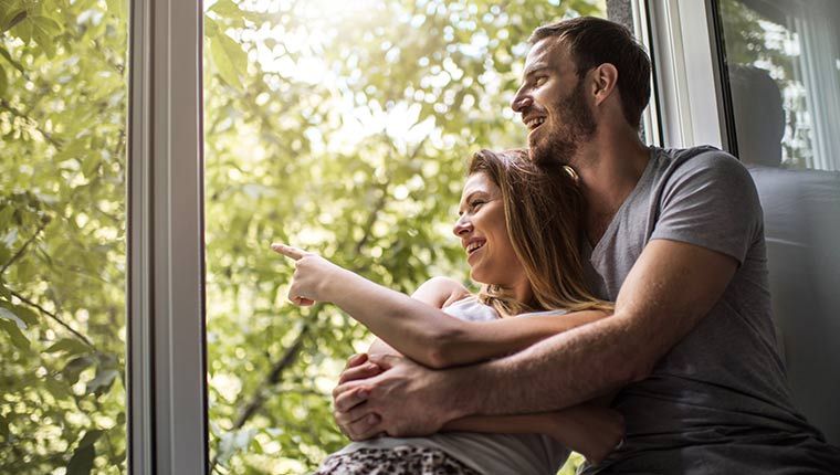 A couple sitting in the window of their home, breathing fresh air.
