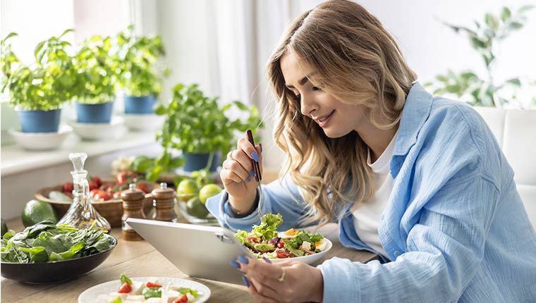 A woman eating a vegan meal checks her health test results on a tablet.