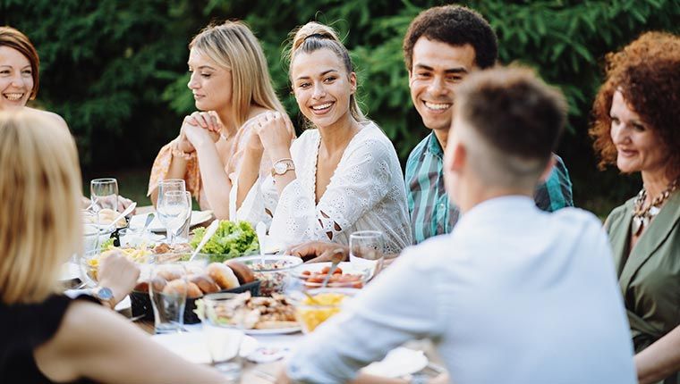 People gathered around an outdoor dining table enjoying a meal in a garden setting.