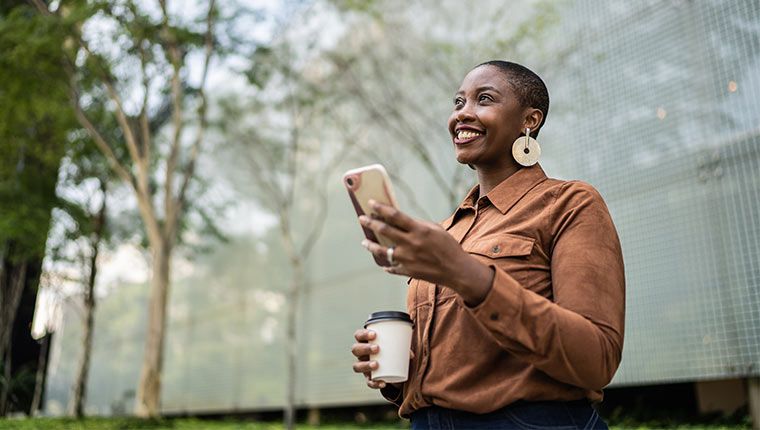 A woman smiles holding her phone outside after checking her test results.