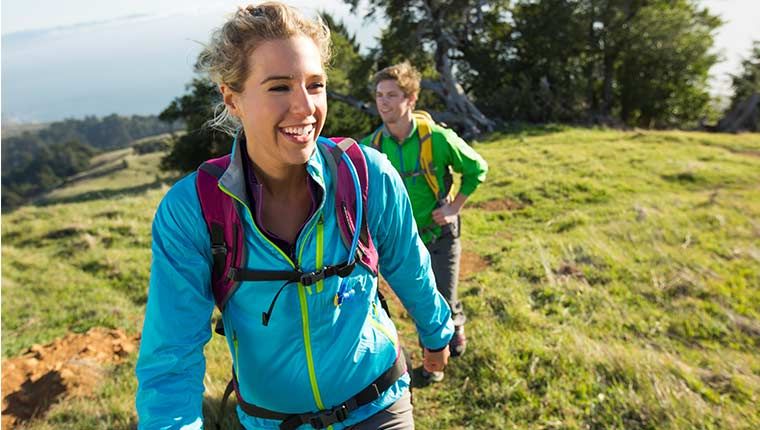 A man and woman happily hike outside in the grass.