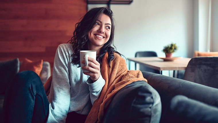 A woman smiles while resting and drinking tea while having mono.