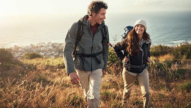 A man and woman are outside hiking and smiling.