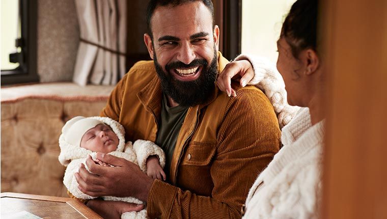 A man smiles while holding a newborn baby.
