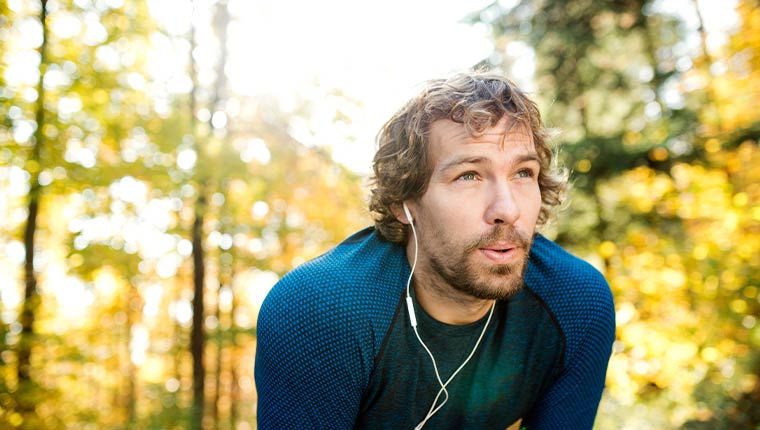 A man takes a short break from running while listening to headphones.